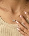 Person wearing round & emerald cut lab diamond solitaire pendant necklace in yellow gold.
