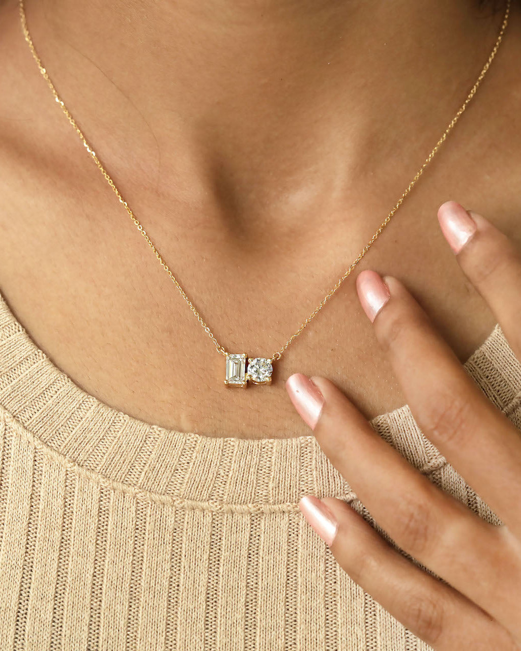 Person wearing round & emerald cut lab diamond solitaire pendant necklace in yellow gold.
