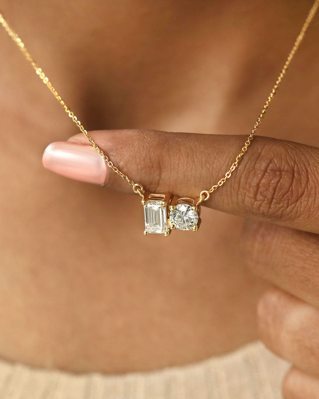 Person wearing round & emerald cut lab diamond solitaire pendant necklace in yellow gold.