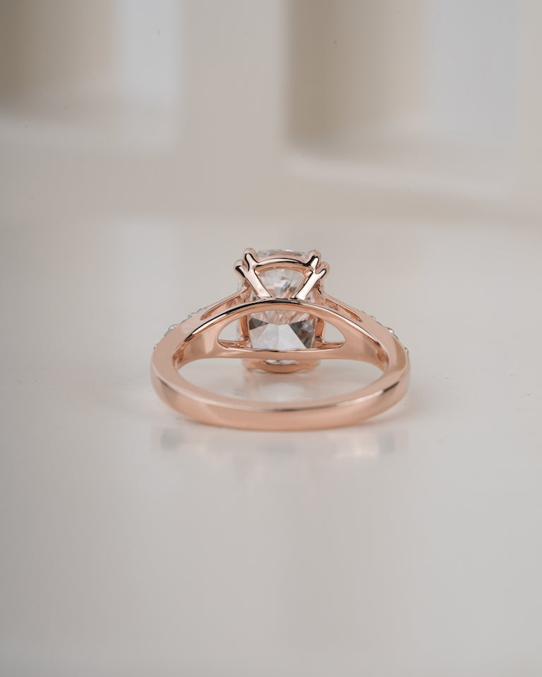 A rose gold ring with a clear round-cut gemstone in a four-prong setting, resting on a light beige surface.