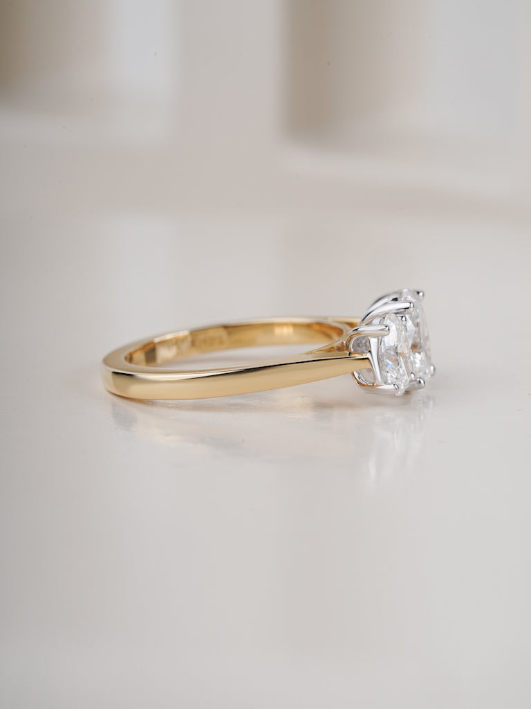 A classic solitaire engagement ring featuring a round brilliant-cut clear gemstone in a four-prong setting on a polished yellow gold band, photographed on a clean, light beige reflective surface.