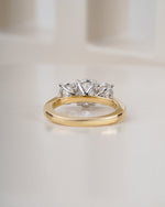 A yellow gold ring band with a three-stone diamond engagement ring set in silver, displayed on a clean white surface.
