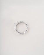A silver-toned eternity ring set with small clear stones, photographed against a plain light gray background.