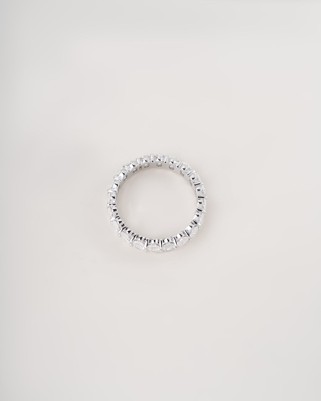 A silver-toned eternity ring set with small clear stones, photographed against a plain light gray background.
