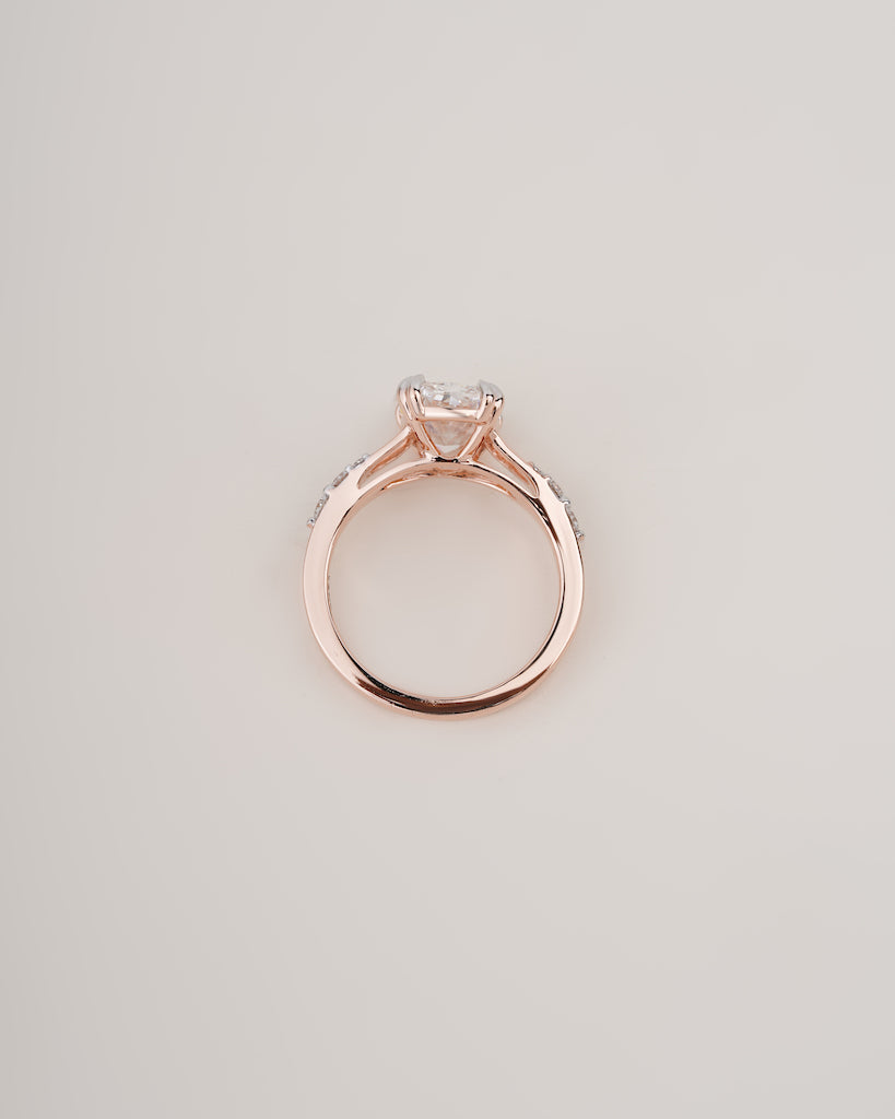 A rose gold ring with a heart-shaped clear gemstone in a four-prong setting, shown from a top-down view on a light gray background.