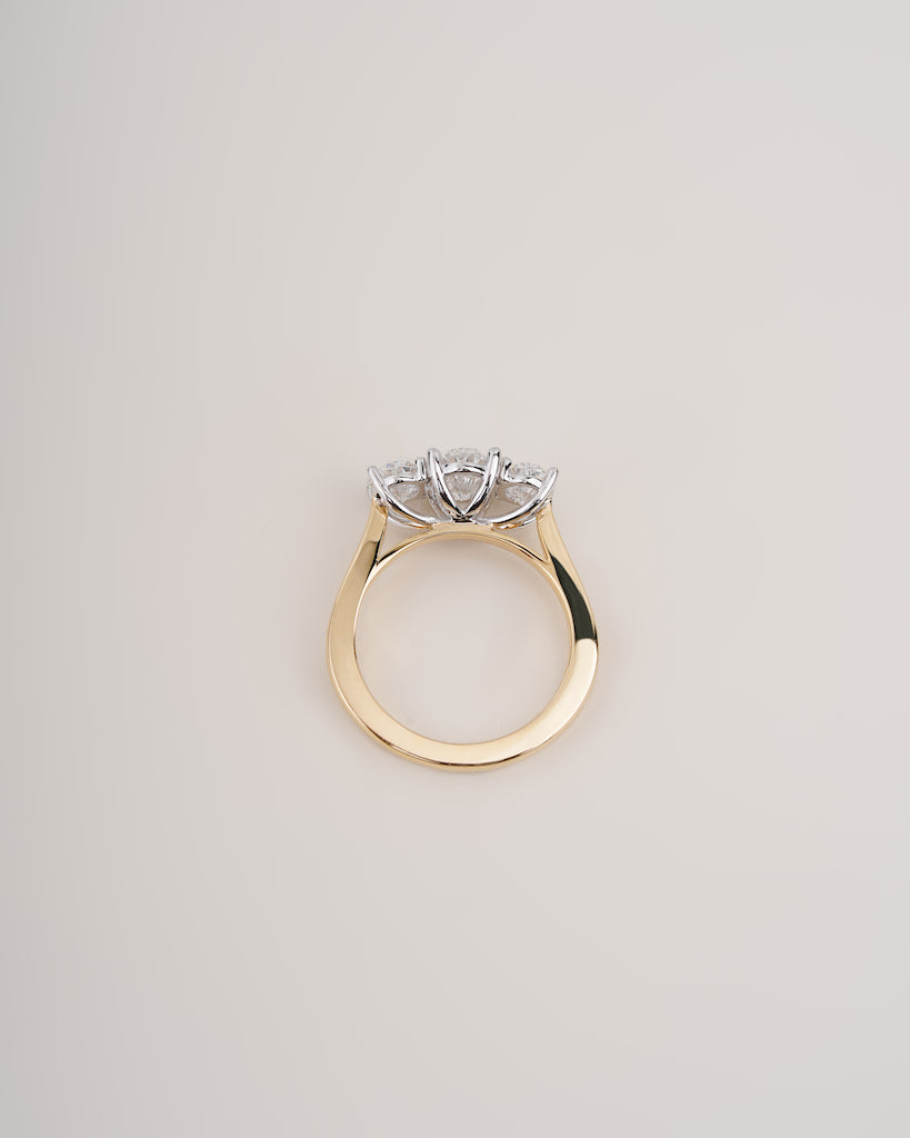 A gold ring with a three-stone cluster setting featuring clear gemstones, photographed from a top-down angle on a light beige background.