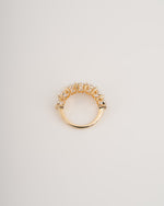 A gold ring with a curved top set with small clear stones, photographed on a plain light gray background.