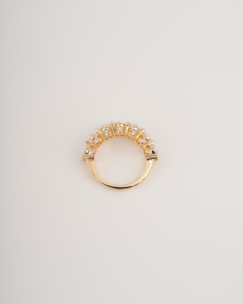 A gold ring with a curved top set with small clear stones, photographed on a plain light gray background.