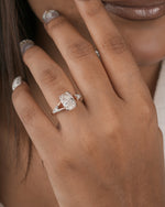 A close-up lifestyle shot of a woman's hand wearing a silver-toned diamond engagement ring with a marquise-cut center stone and smaller side stones.