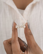 A close-up of a person's hand holding a diamond eternity ring with a gold band, set against a soft white shirt background.