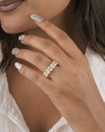 A close-up of a woman's hand wearing a silver band ring set with clear round gemstones, styled with silver and white nail art.