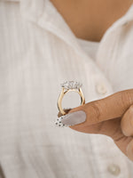 A close-up of a hand holding a gold ring with a clear diamond solitaire setting, worn on a finger with a white button-up shirt in the background.