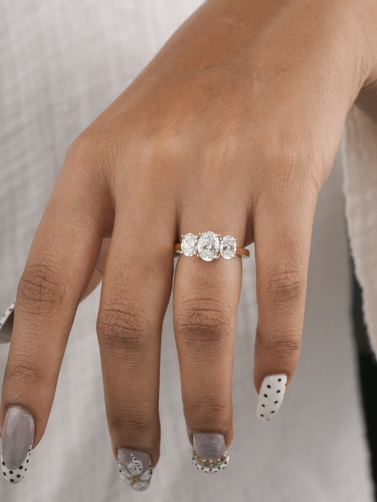A close-up of a hand wearing a three-stone diamond engagement ring. The ring features three round brilliant-cut diamonds set in a yellow gold band.