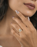 A close-up lifestyle shot of a woman wearing a gold ring with a rectangular clear gemstone on her finger, with her hand resting near her chin.