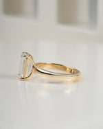 A yellow gold ring with a large rectangular clear baguette-cut gemstone, shown in a side profile on a reflective white surface.