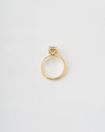 A gold ring with a single bezel-set clear gemstone, photographed from a top-down perspective on a clean white background.