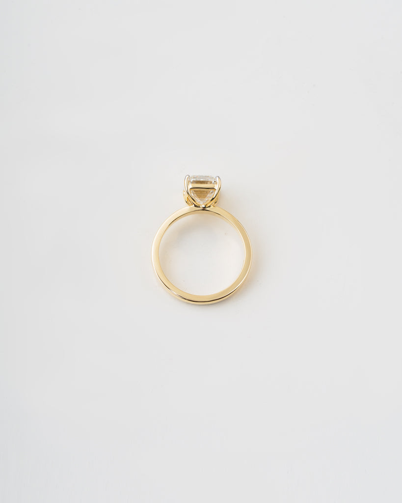 A gold ring with a single bezel-set clear gemstone, photographed from a top-down perspective on a clean white background.