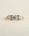 Close up shot of a three stone diamond ring with rose gold band displayed on white background.