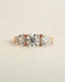 Close up shot of a three stone diamond ring with rose gold band displayed on white background.