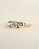 Side view of a three stone diamond ring with rose gold band displayed on white background.