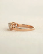 Side view of a three stone diamond ring with rose gold band displayed on white background.