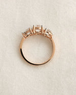 Close up shot of a three stone diamond ring with rose gold band displayed on white background.