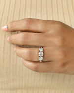 Close up shot of a hand wearing a  three stone diamond ring with rose gold band .