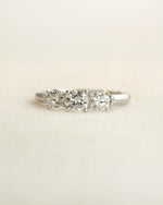 Centered shot of a three stone round cut diamond ring on a light colored background.