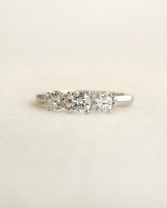 Centered shot of a three stone round cut diamond ring on a light colored background.