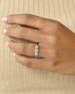 Hand wearing three stone round cut diamond ring .
