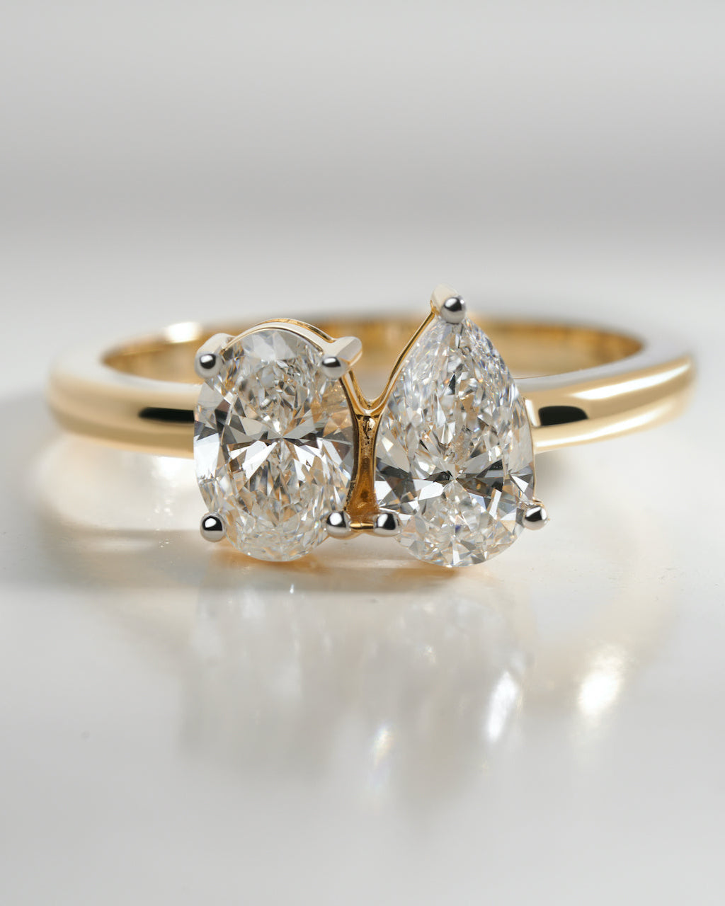 Gold ring with two pear-shaped diamonds on a light background