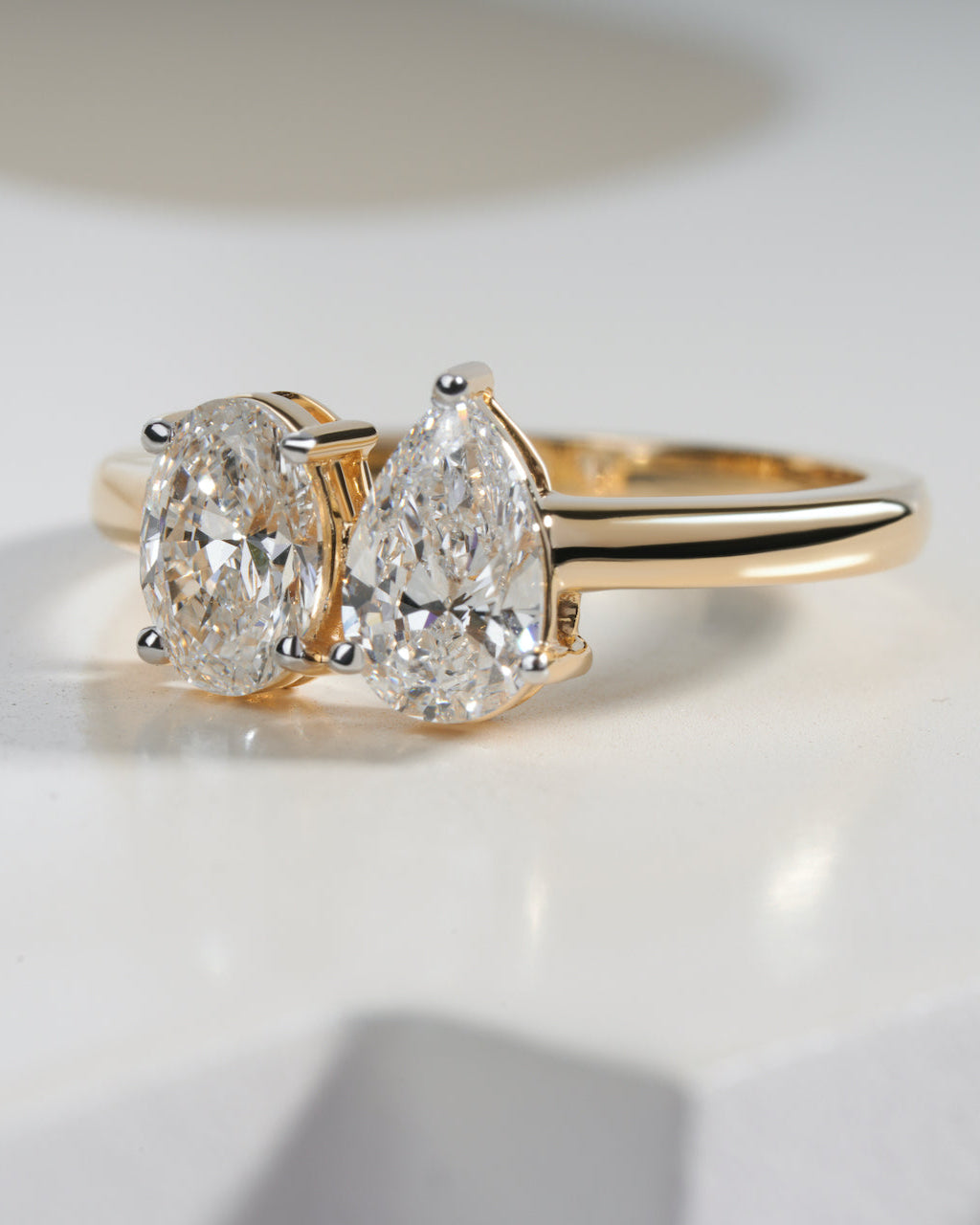 Gold ring with two pear-shaped diamonds on a light background