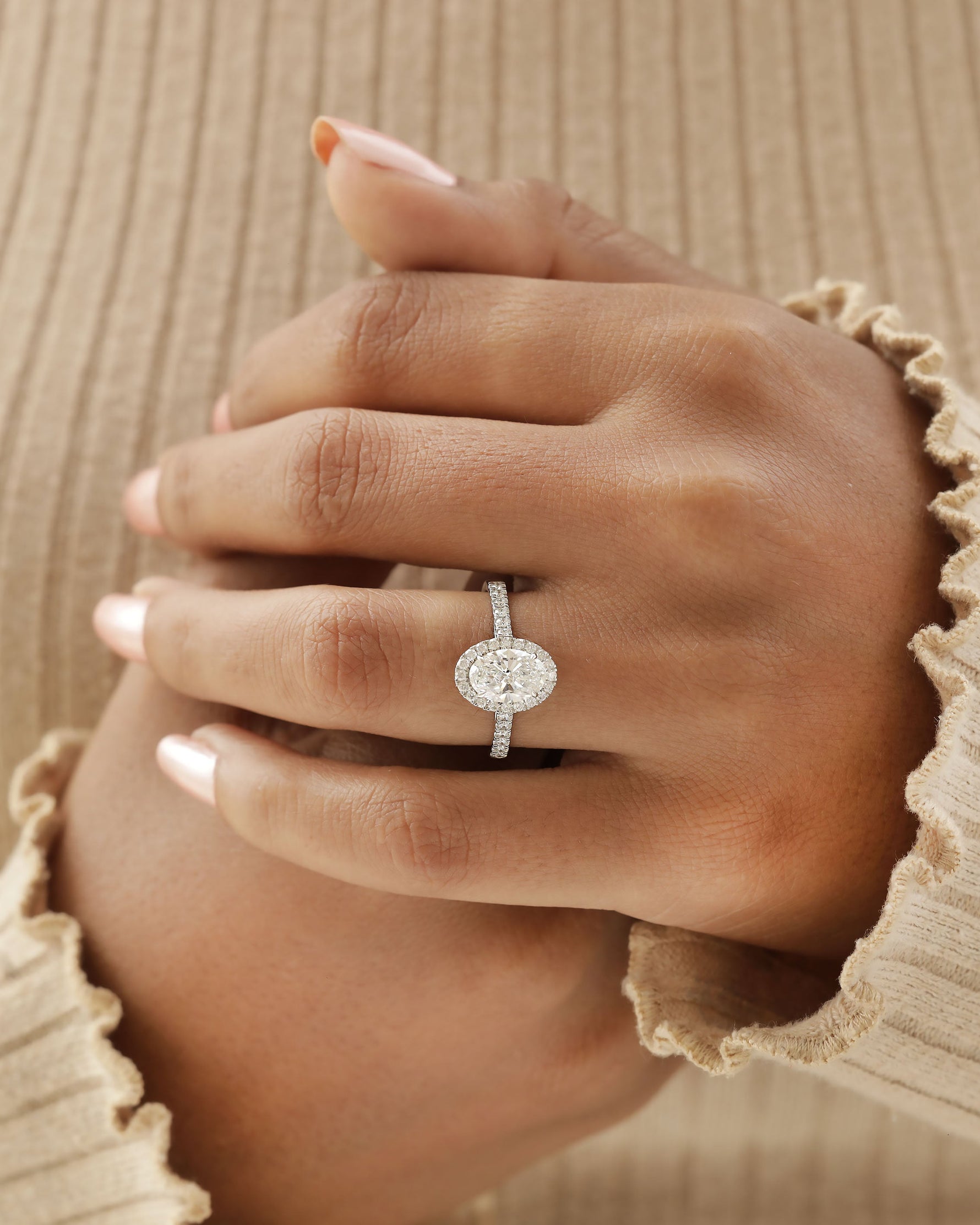 Hand wearing white gold oval halo engagement ring.
