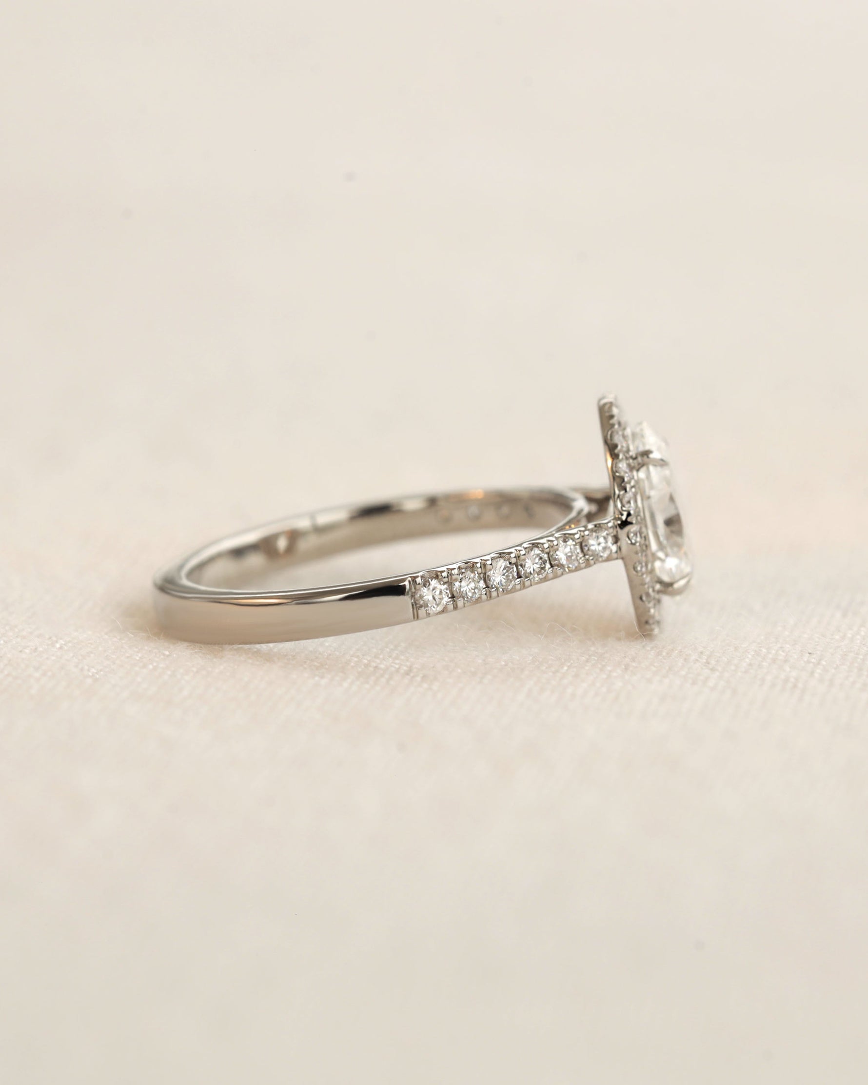 Side view of white gold oval halo engagement ring. 