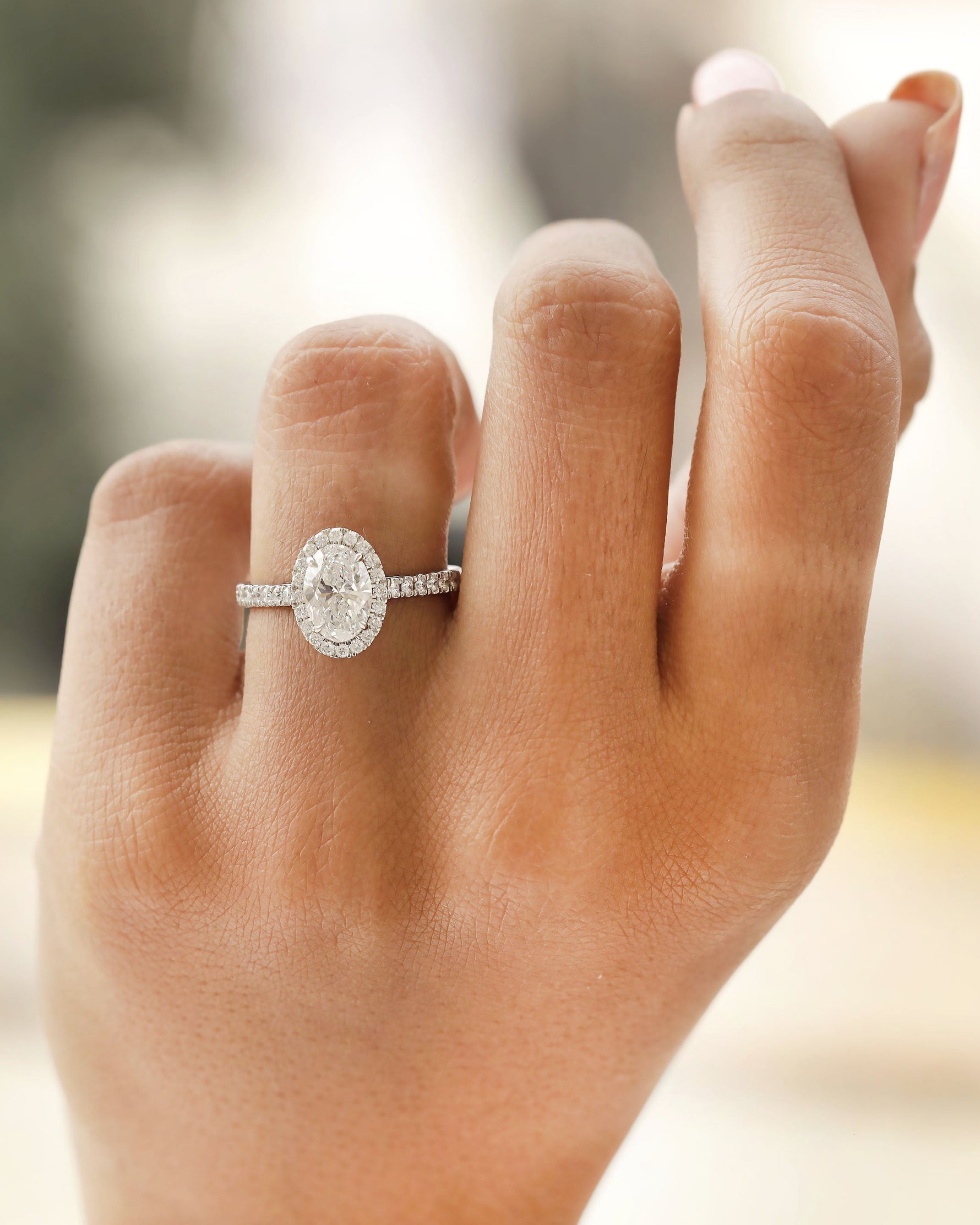 Hand wearing white gold oval halo engagement ring.
