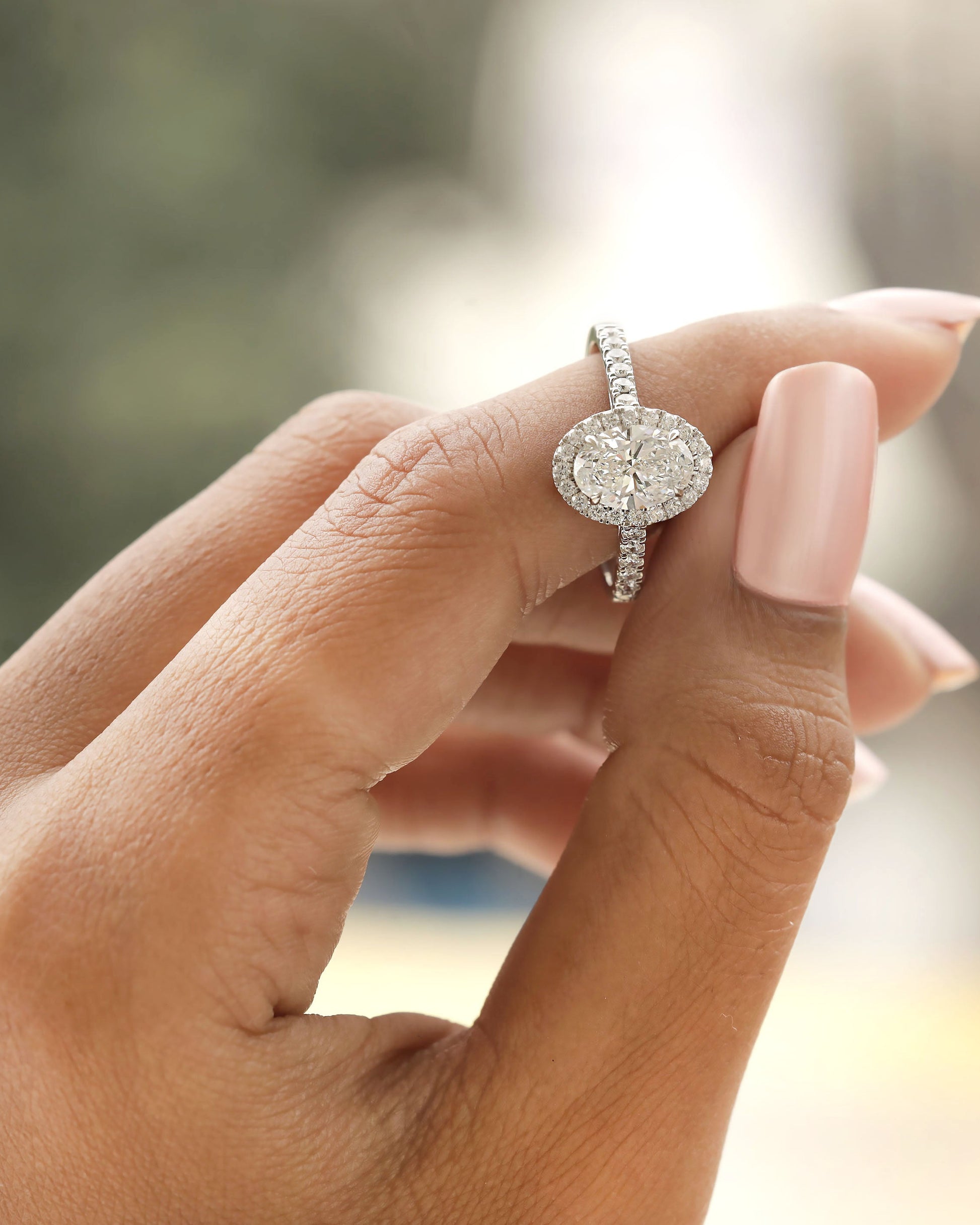 Hand holding white gold oval halo engagement ring.