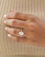 Hand wearing white gold oval halo engagement ring.
