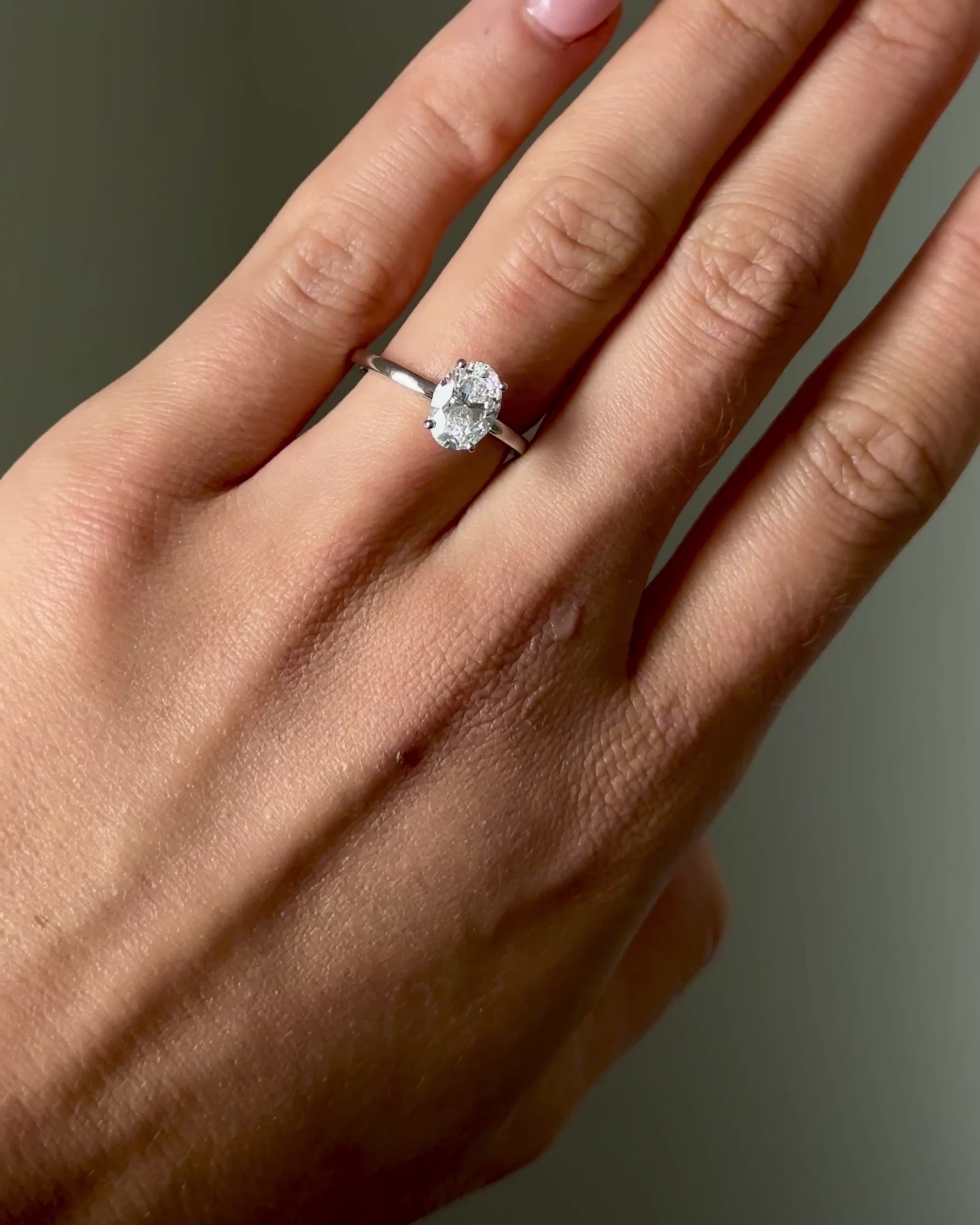 Hand wearing a diamond ring on a neutral background
